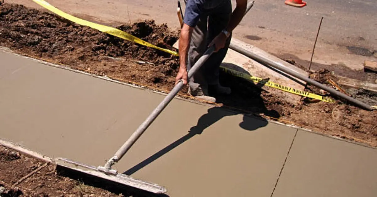 Worker using magnesium bull float on freshly poured concrete slab