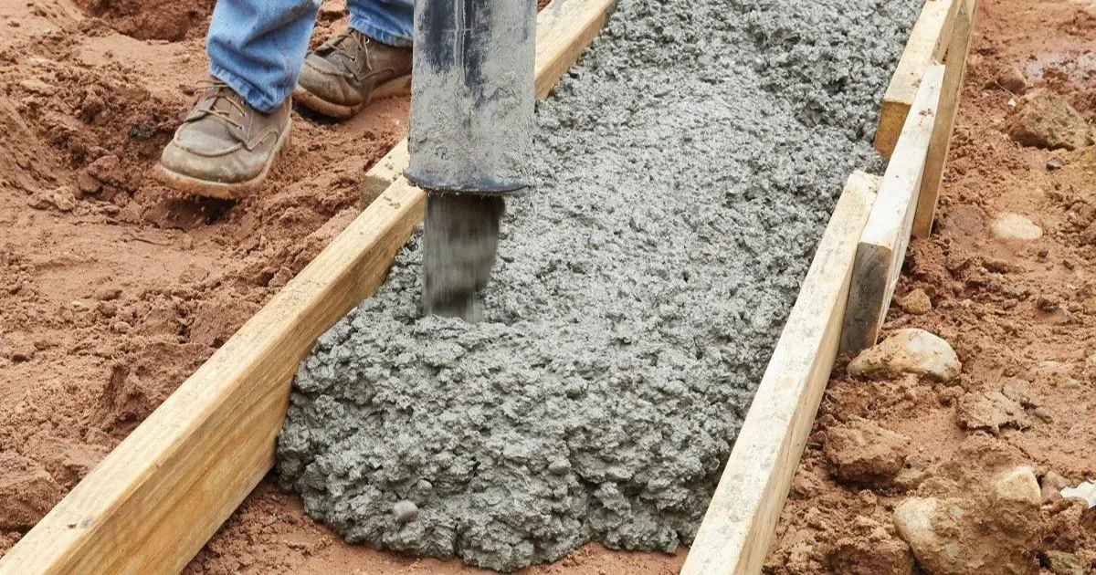 Construction crew guiding concrete from delivery chute into footing forms